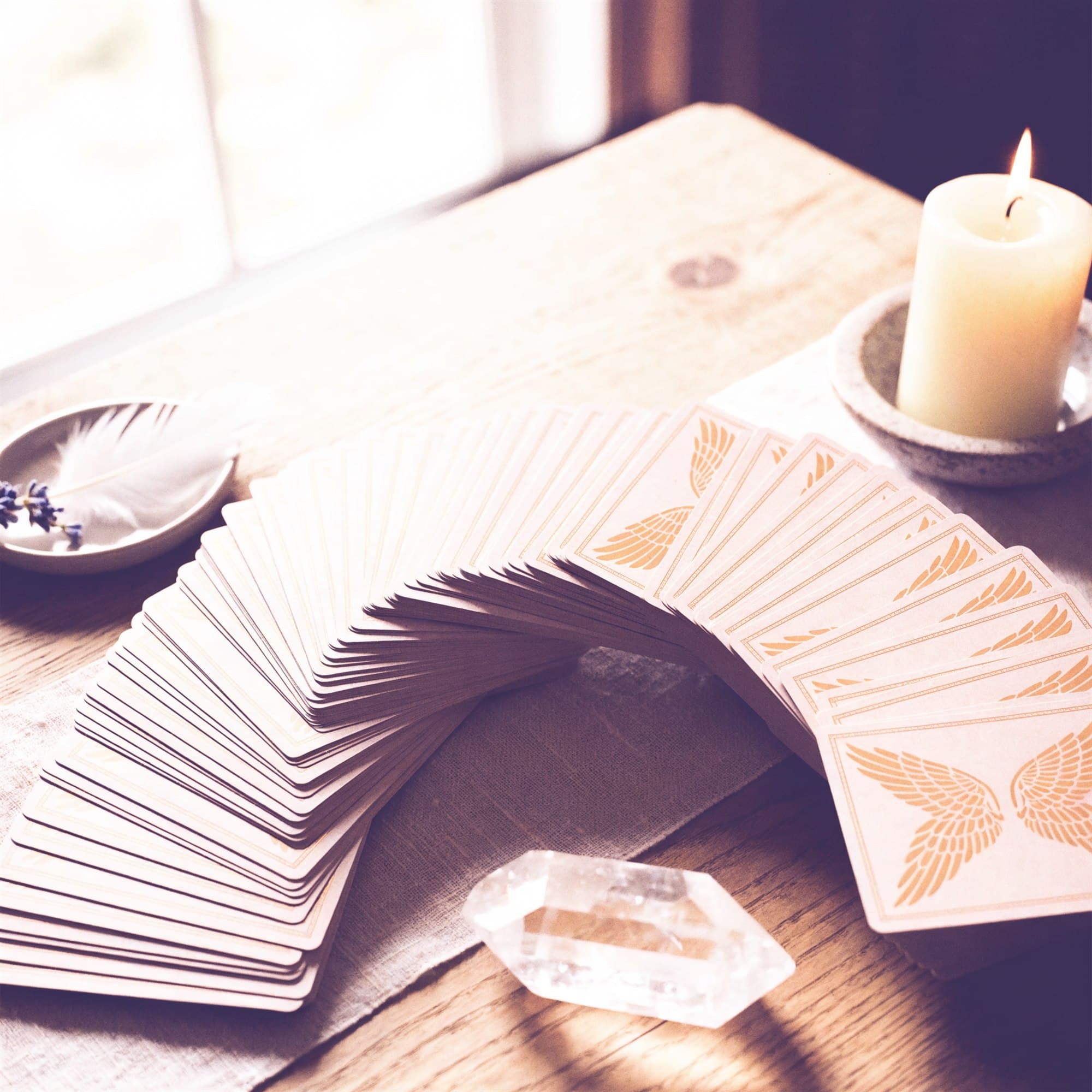 An angel oracle deck fanned in an arc across a wooden table beside a candle and clear quartz